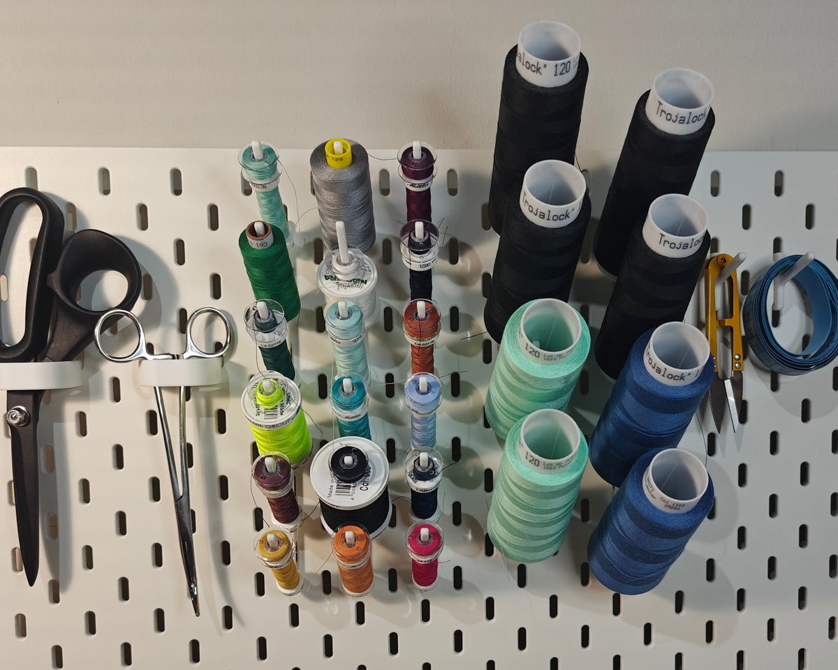 Een foto van het middelgrote naaigaren en lockgaren pakket. Op de foto zie je ge3dprinte artikelen. Twee haken voor een schaar, twee haken voor andere artikelen (zoals een draadknipper, liniaal, meetlint enz) en 6 haken met elk 3 klosjes naaigaren met een spoeltje bij sommige daarnaast ook 4 haken met elk 2 klossen lockgaren.