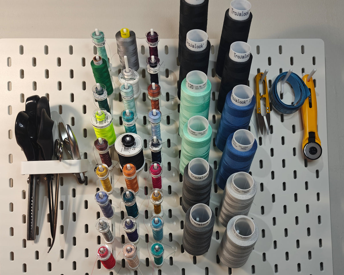 Een foto van het grote naaigaren en lockgaren pakket. Op de foto zie je ge3dprinte artikelen. Een haak voor vier scharen, drie haken voor andere artikelen (zoals een draadknipper, liniaal, meetlint enz) en 9 haken met elk 3 klosjes naaigaren met een spoeltje bij sommige daarnaast ook 6 haken met elk 2 klossen lockgaren.