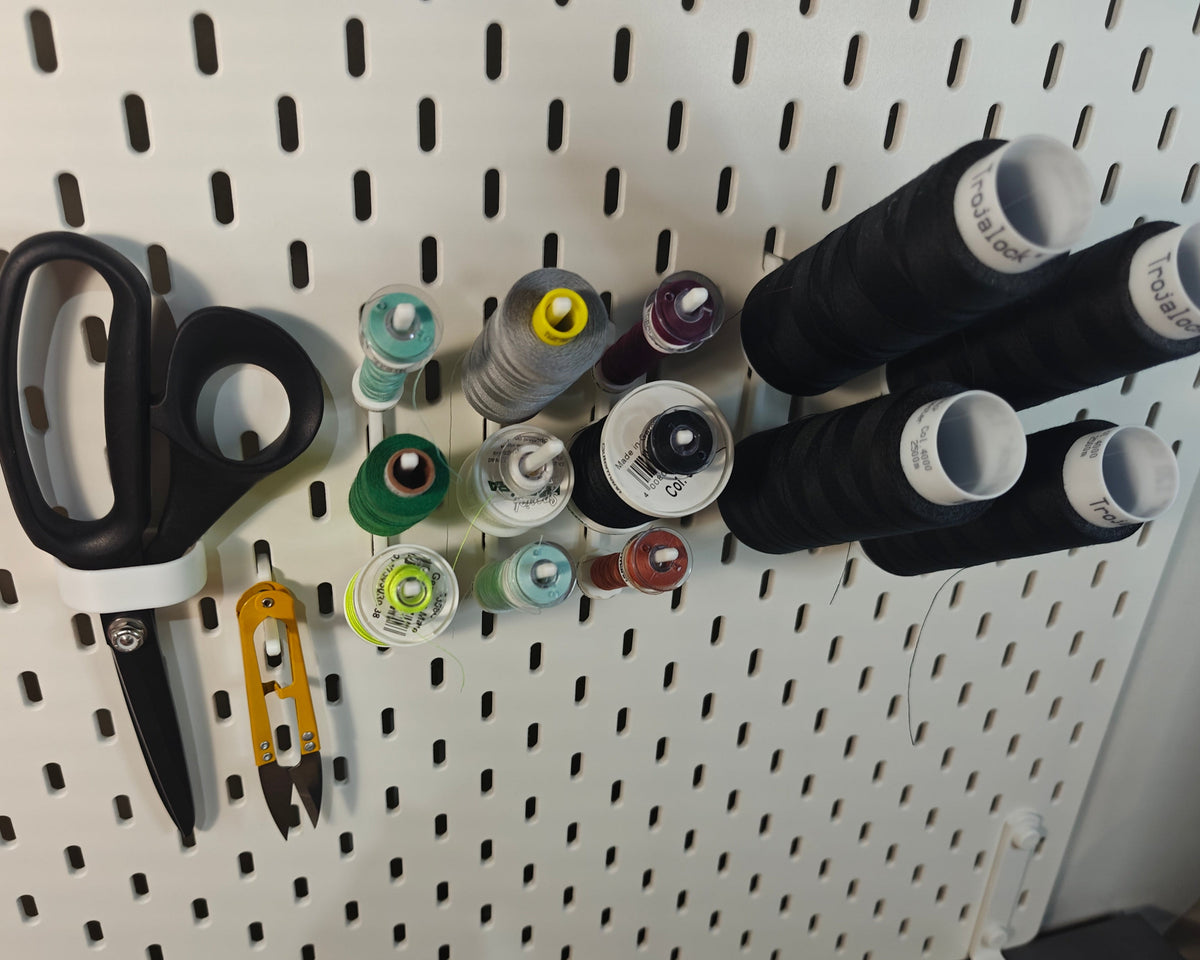 Een foto van het kleine naaigaren en lockgaren pakket. Op de foto zie je ge3dprinte artikelen. Een haak voor een schaar, een haak voor andere artikelen (zoals een draadknipper, liniaal, meetlint enz) en 3 haken met elk 3 klosjes naaigaren met een spoeltje bij sommige daarnaast ook 2 haken met elk 2 klossen lockgaren.