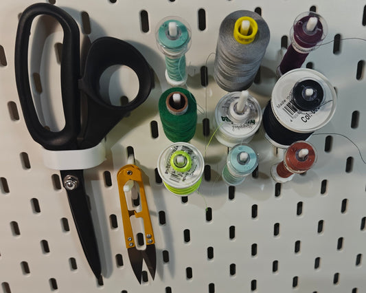 Een foto van het kleine naaigaren pakket. Op de foto zie je ge3dprinte artikelen. Een haak voor een schaar, een haak voor andere artikelen (zoals een draadknipper, liniaal, meetlint enz) en 3 haken met elk 3 klosjes naaigaren met een spoeltje bij sommige.